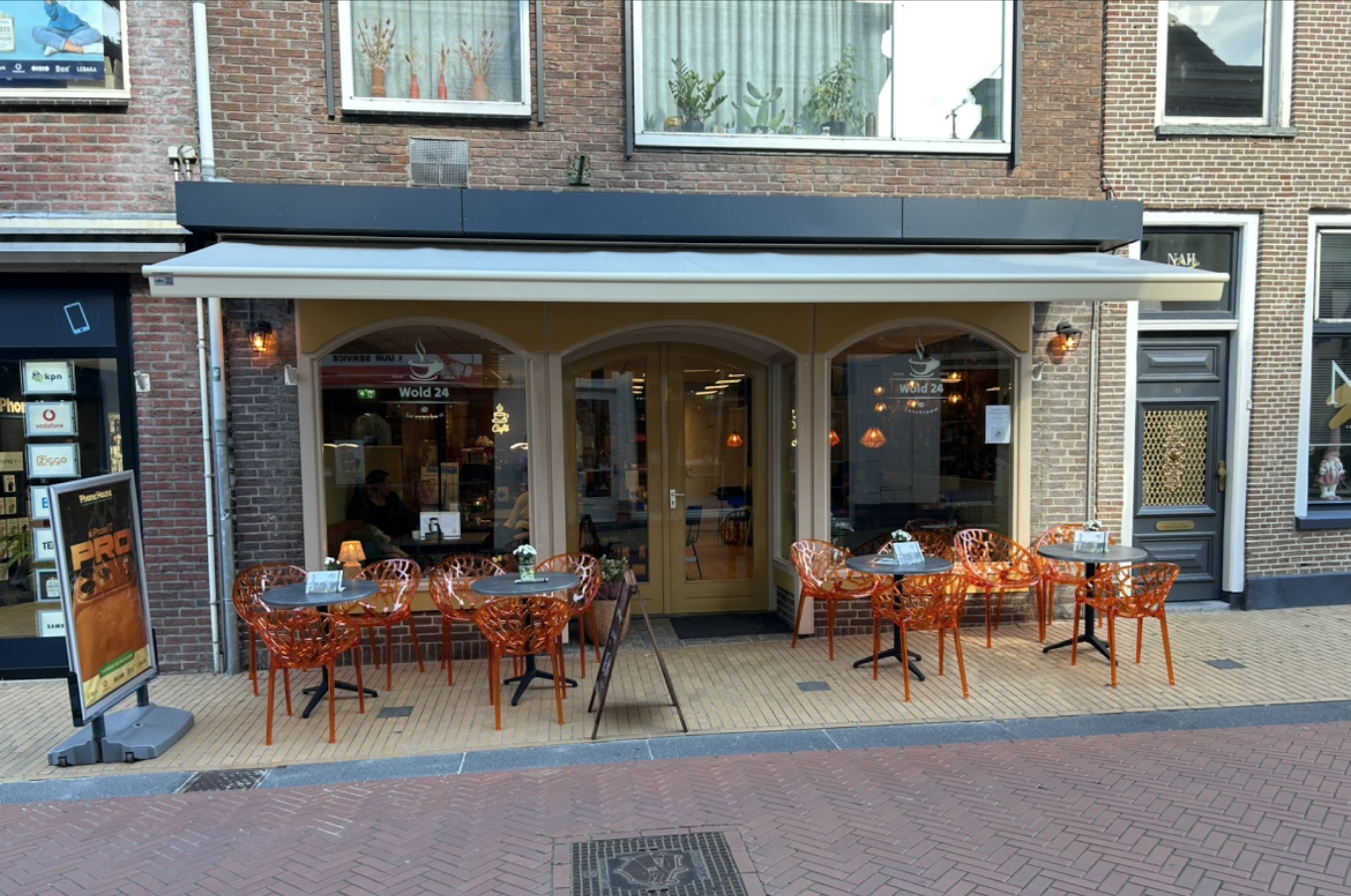 Terras van Wold24 met houten pui en oranje stoelen aan de Woldpromenade in Steenwijk
